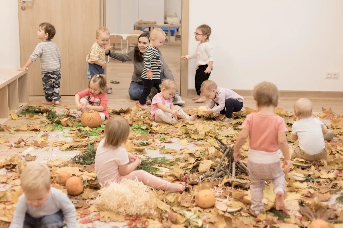 Grupa dzieci podczas zabawy w jesiennych liściach w ogrodzie MOC Montessori